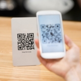 Closeup of a hand holding phone and scanning qr code. Woman hand paying with qr code. Close up of customer hand making payment through smart phone and scan code.